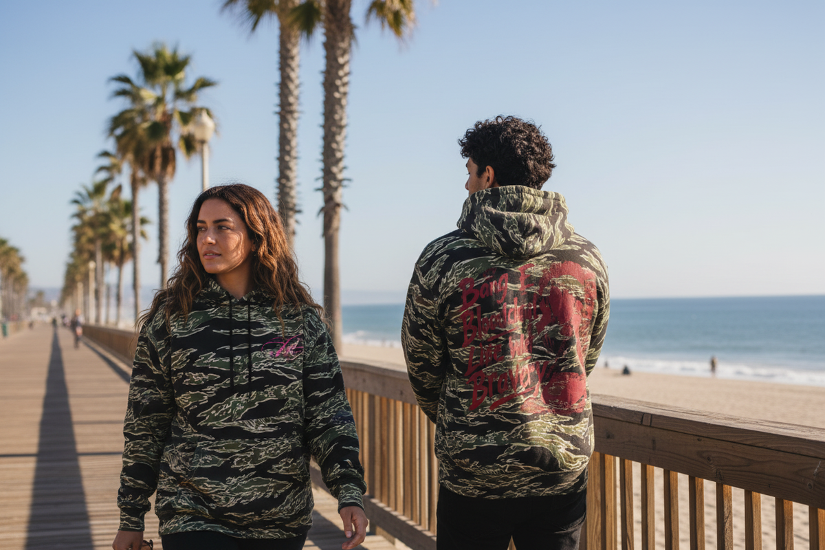 A woman and a man in a tiger camo hoodie on a sunny boardwalk, back graphic visible